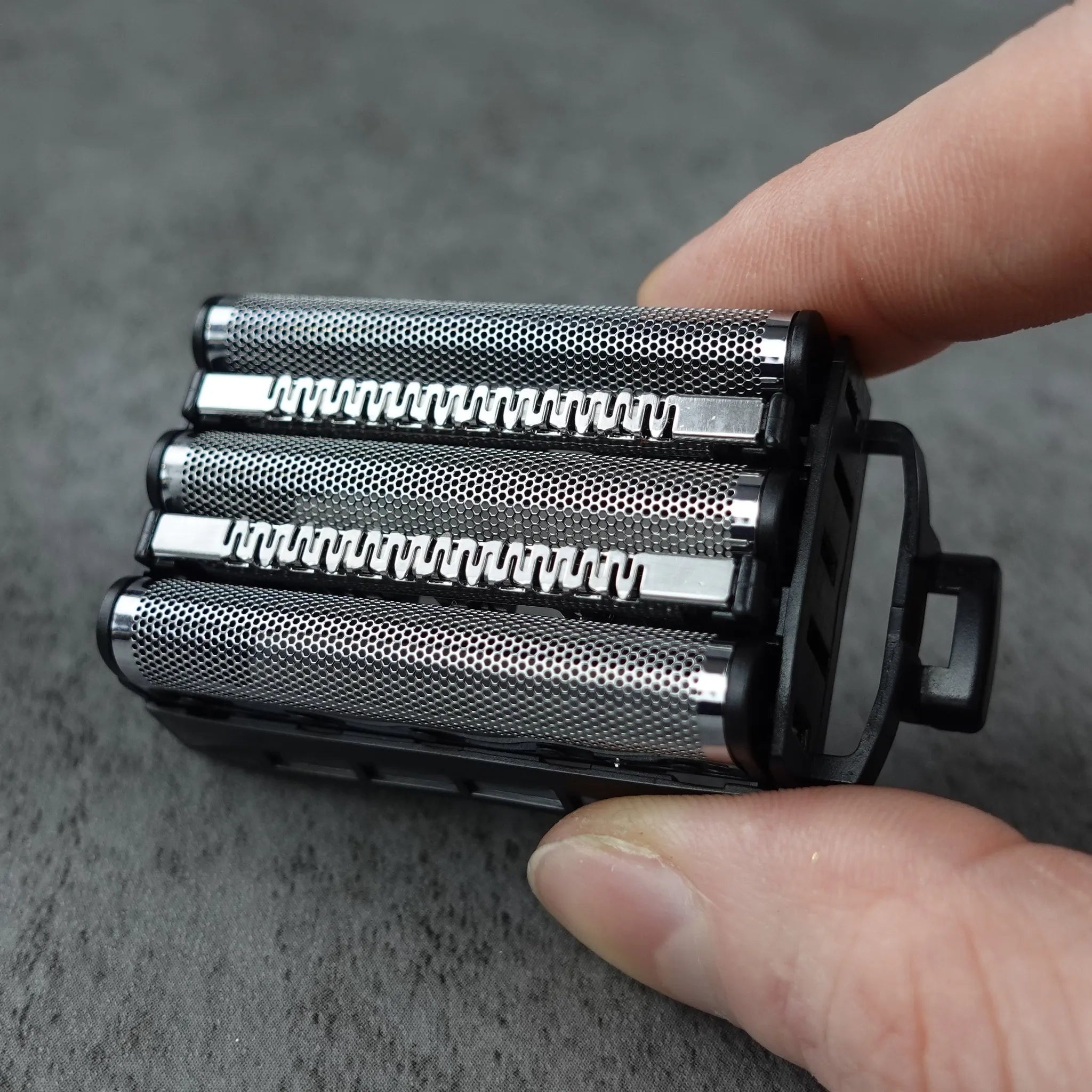 Hand holding a black electric shaver head on a gray surface
