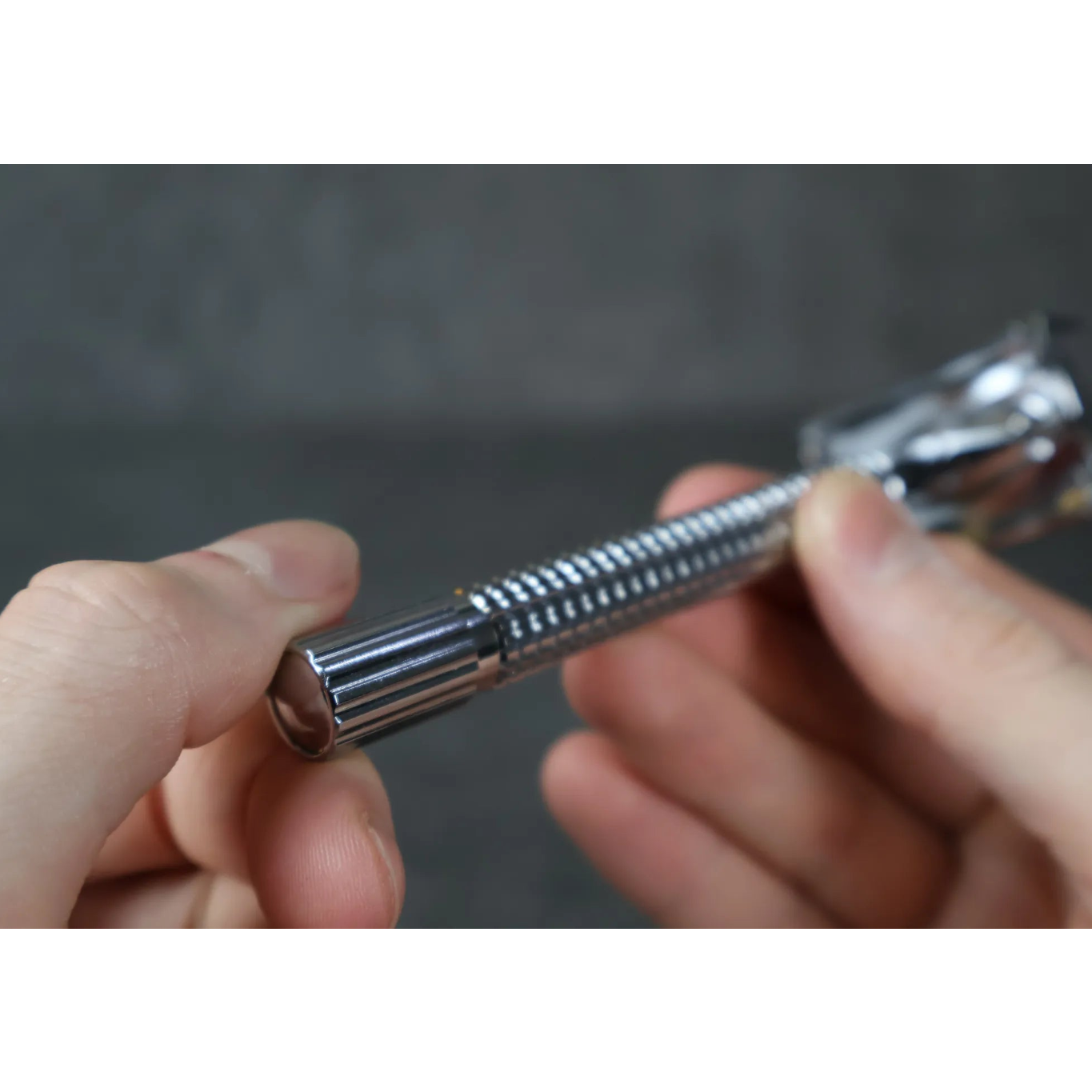 Close-up of a hand holding a safety razor handle against a dark background
