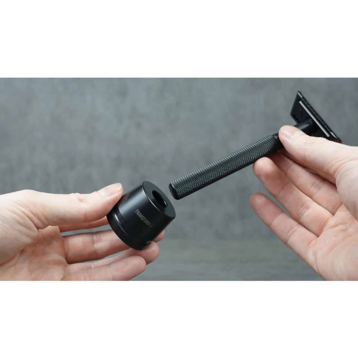Two hands holding a black safety razor against a gray background