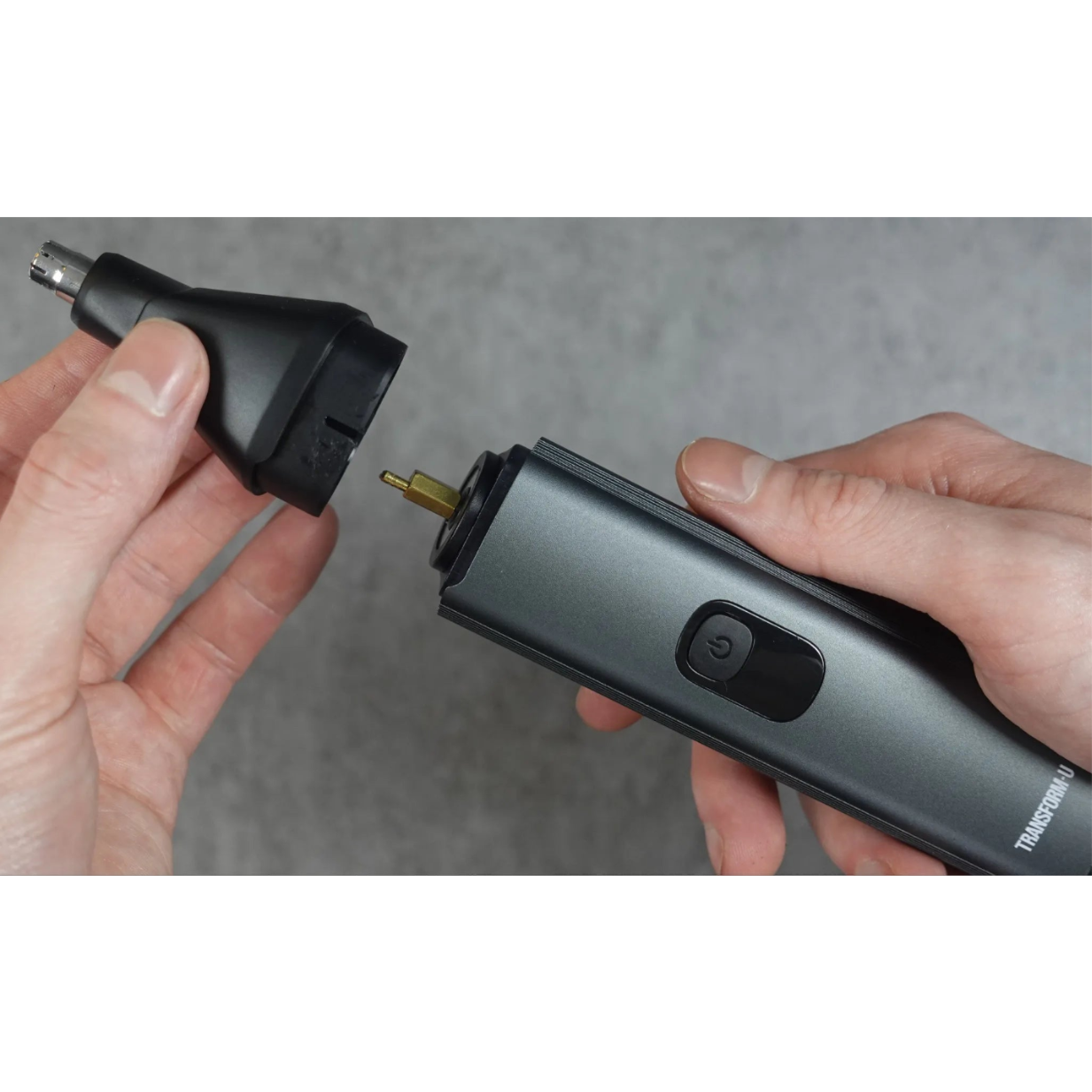 Person holding a black hair trimmer with a small attachment, against a gray background