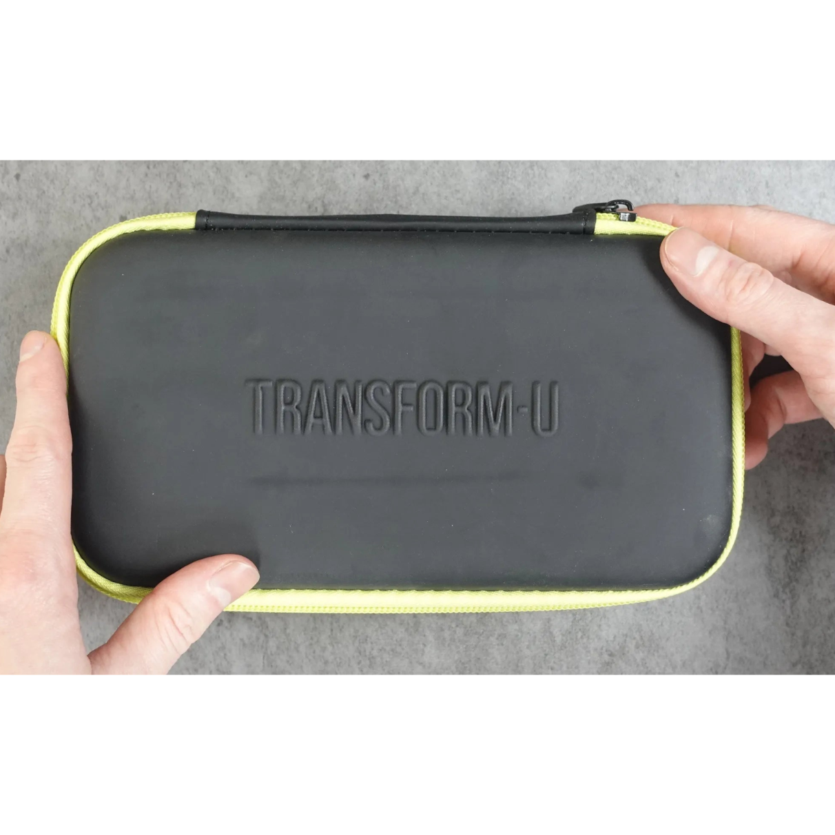 Black carrying case with 'TRANSFORM-U' branding held by hands on a gray background
