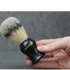 Hand holding a black shaving brush with gray bristles against a gray background