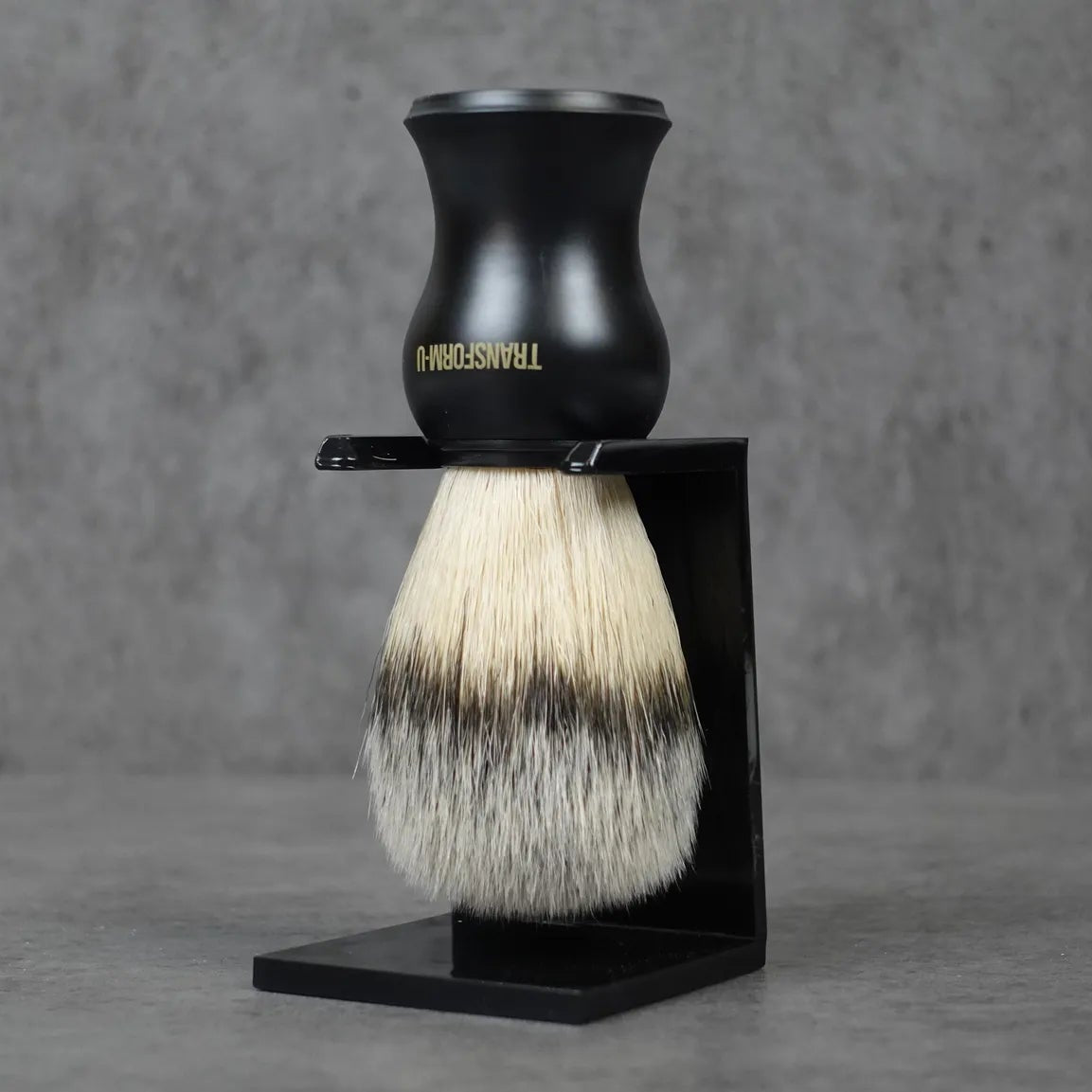 Shaving brush with black handle and stand on a gray background