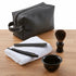 Set of grooming tools including a black leather pouch, comb, straight razor, towel, and shaving brush on a wooden surface.