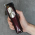 Hand holding a maroon hair clipper against a gray background