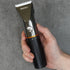 a black hair clipper being held by a hand against a grey background
