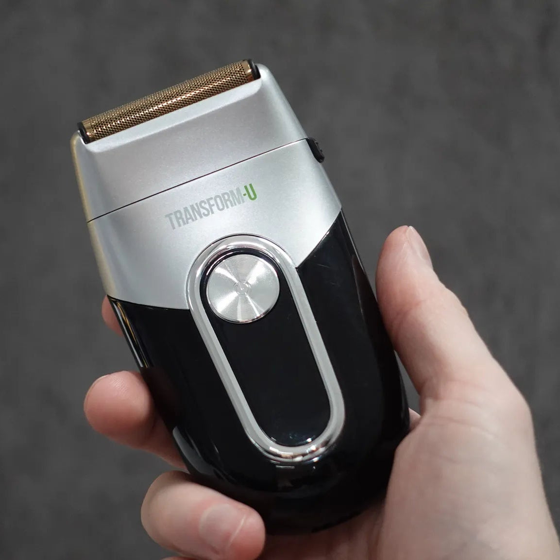 Hand holding a black and silver electric shaver against a dark background